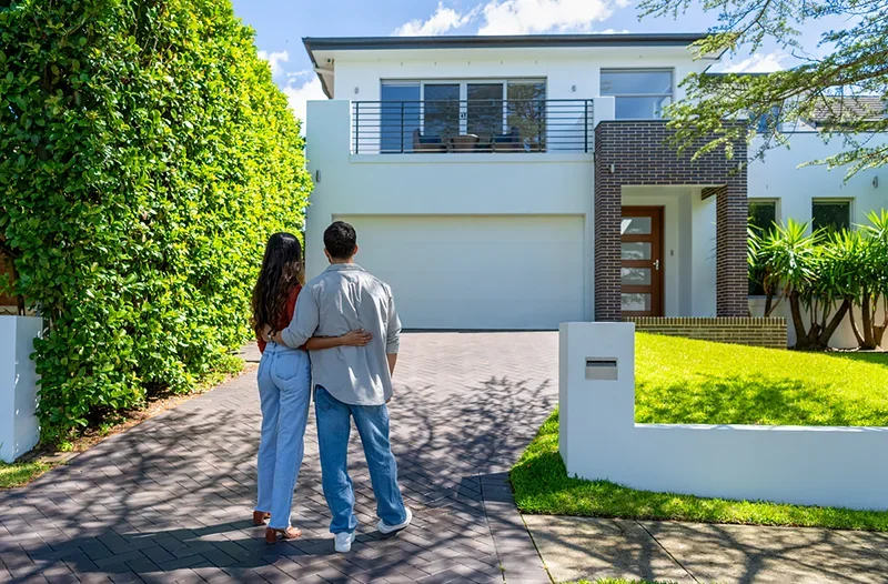 A couple standing in front of their first house that they bought with kiwisaver - social