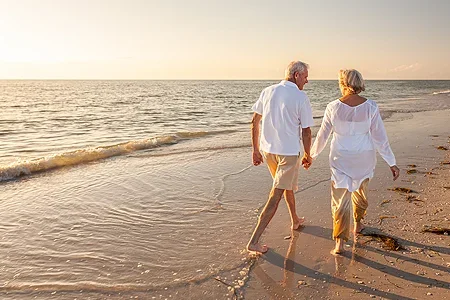 A retired couple walking on the beach hand in hand - listing