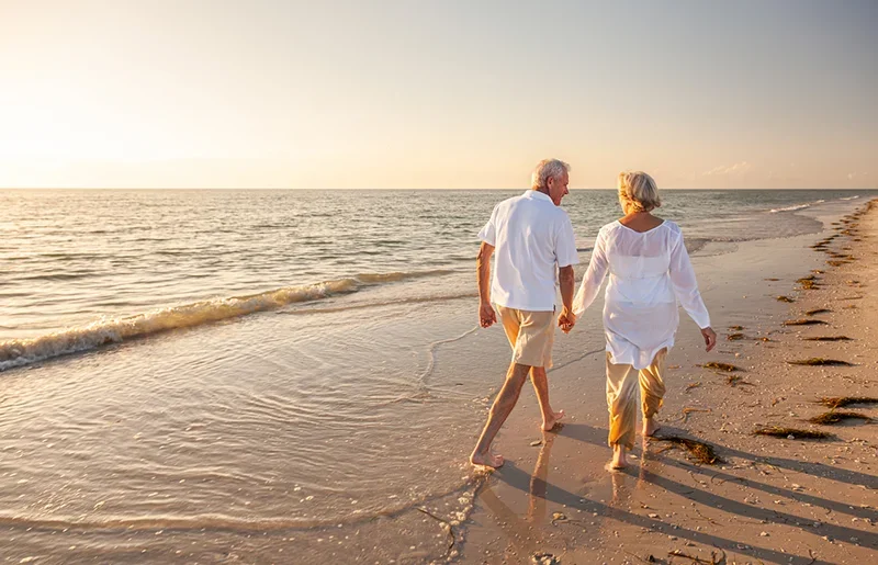 A retired couple walking on the beach hand in hand