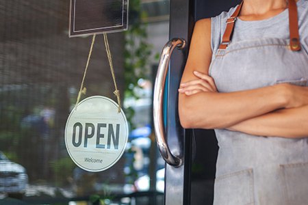 Small business owner standing next to open for business sign