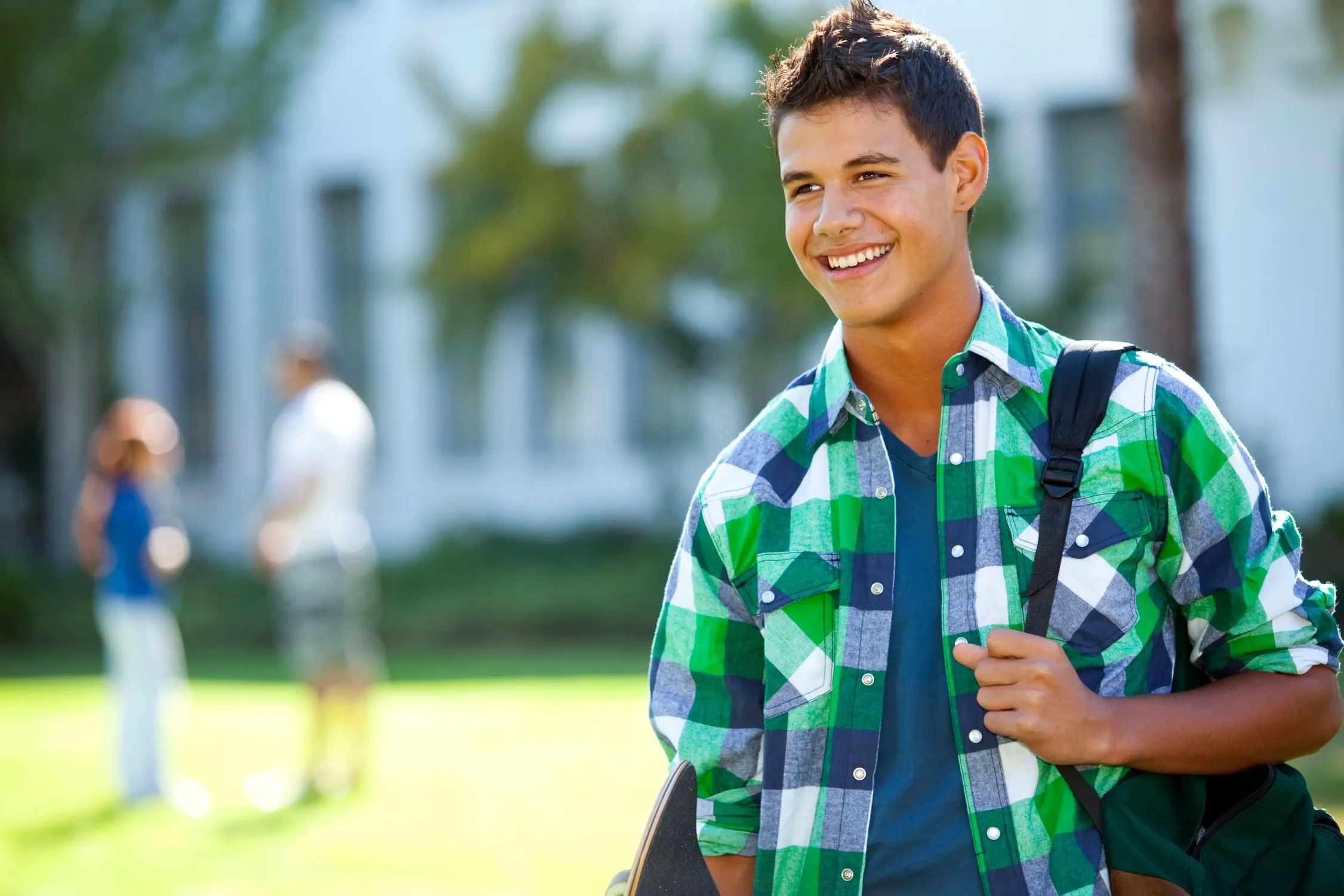 Young boy smiling standing in a grassy field with a backpack on