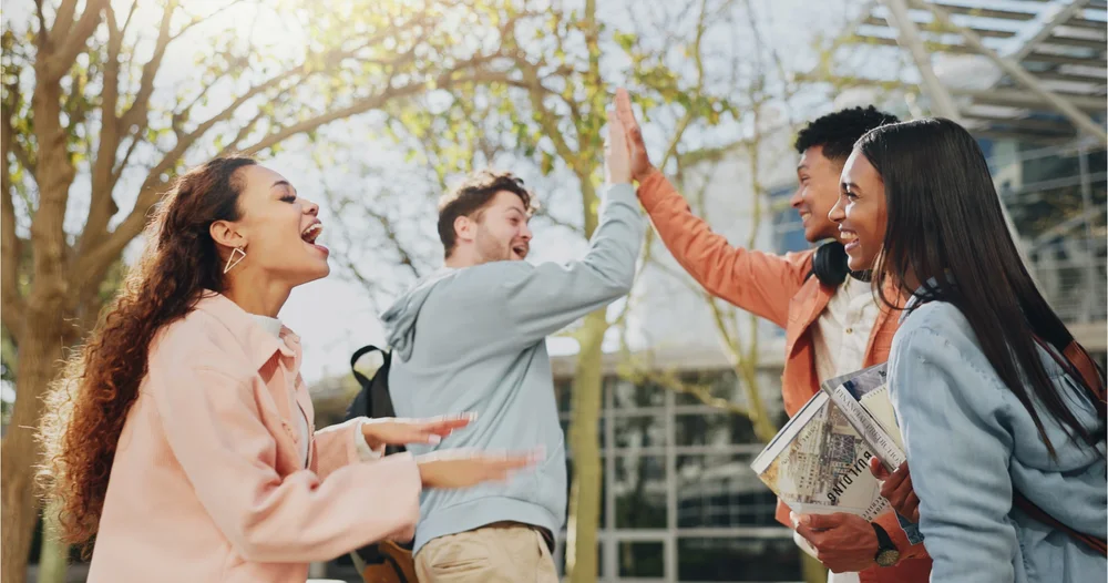 a group of four students enjoying themselves. two of them highfive.