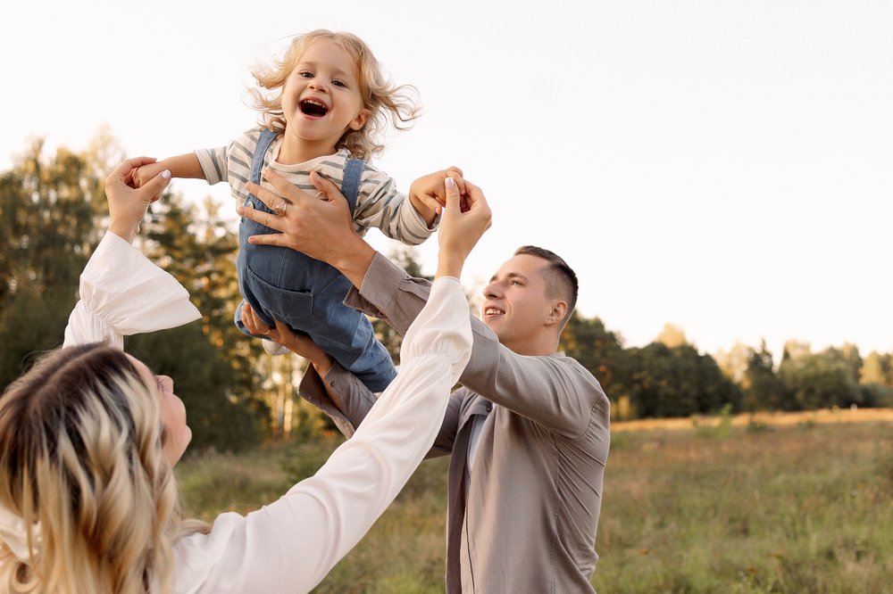 small child being thrown gleefully in the air by her parents
